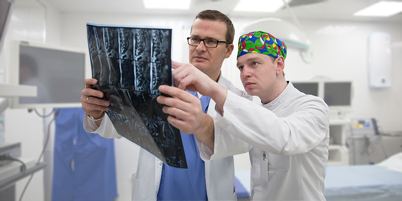 врачи онкологи Европейской клиники в операционной со снимком КТ позвоночного столба